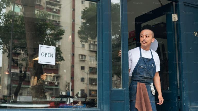 Small shop owner standing by an Open sign
